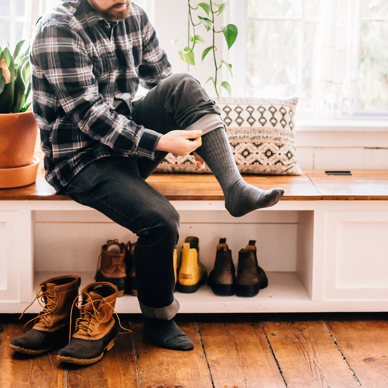 Darn Tough The Standard Mid-Calf Lightweight Lifestyle Socks in charcoal gray with ribbed detail, worn by man sitting indoors.