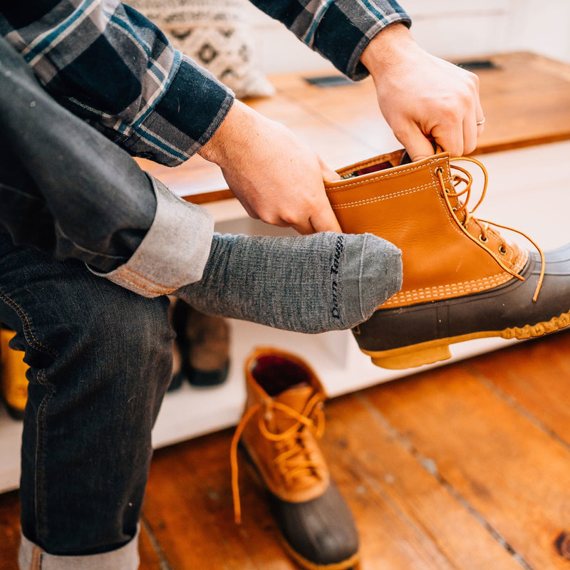 Darn Tough The Standard Mid-Calf Lightweight Lifestyle Socks in gray worn while putting on tan waterproof boots.