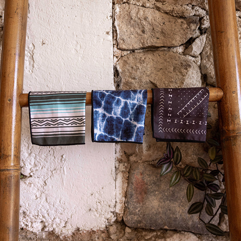 Nomadix Tiny Towel 3-Pack with geometric, tie-dye, and patterned designs in multicolor, hanging on a bamboo ladder.
