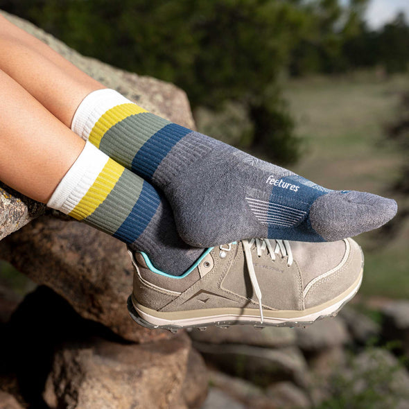 Feetures Trail Max Cushion Mini Crew Sock in gray with colorful blue, green, yellow, and white stripes, worn outdoors.